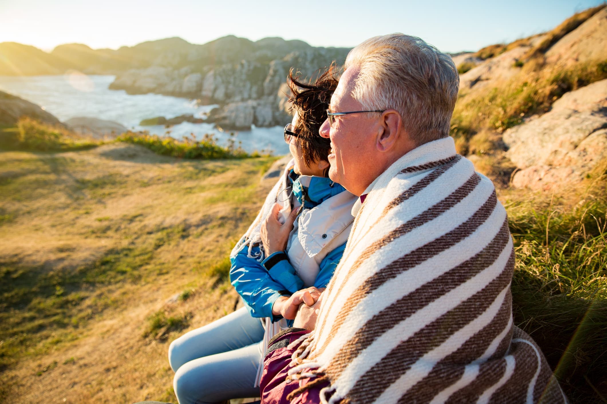 Eldre ektepar sitter tett sammen på kystklippene i Lindesnes ved solnedgang. Brukt som illustrasjon i artikkel om arv for ektefelle uten barn