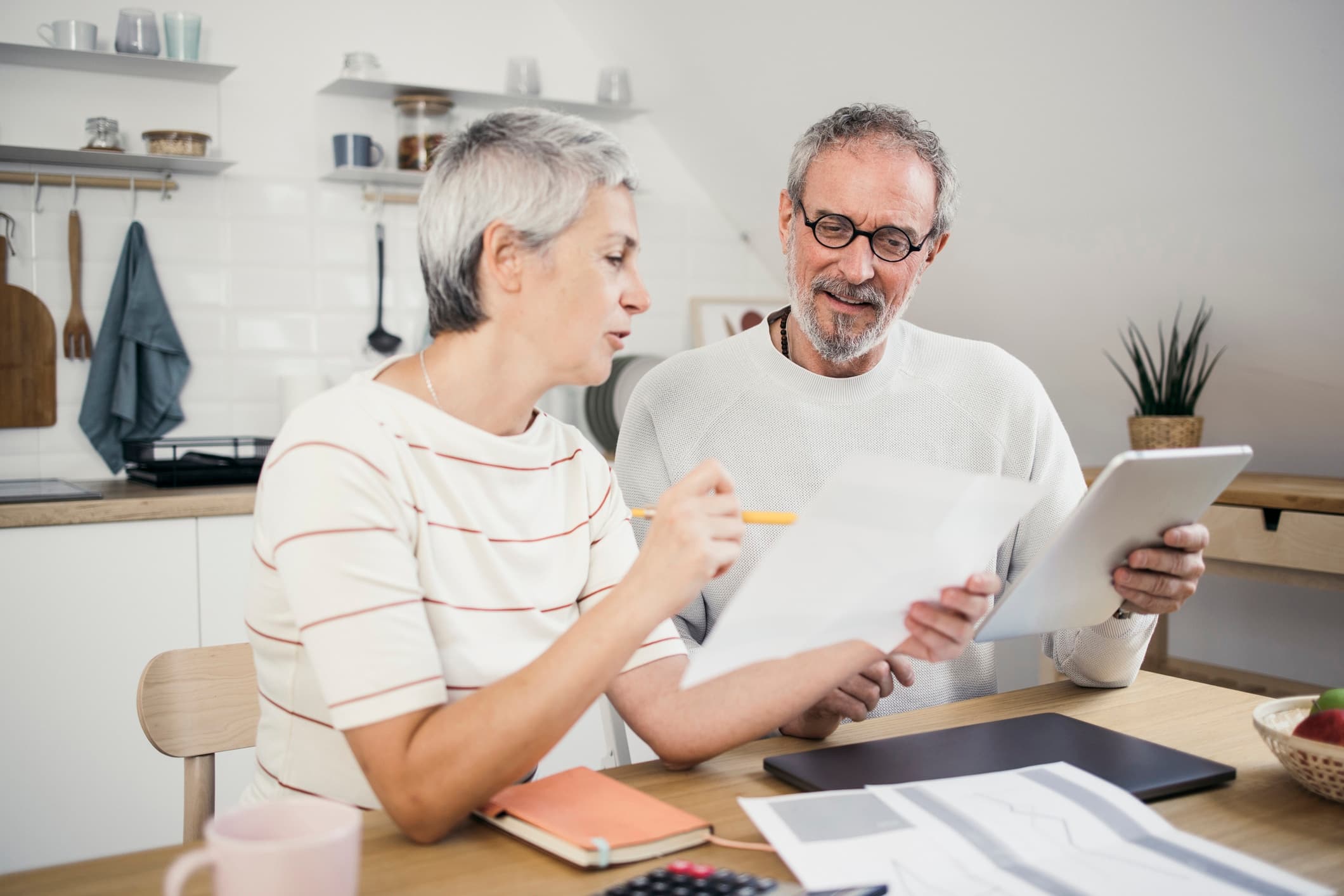 Eldre samboerpar gjennomgår dokumenter ved kjøkkenbordet mens de planlegger testament for samboere og diskuterer arvefordeling.