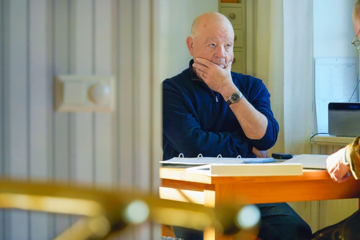 Ettertenksom eldre mann holder hånden mot haken mens han sitter i et møte, illustrerer bekymringer rundt skjevdeling av arv og økonomiske konsekvenser ved skilsmisse.